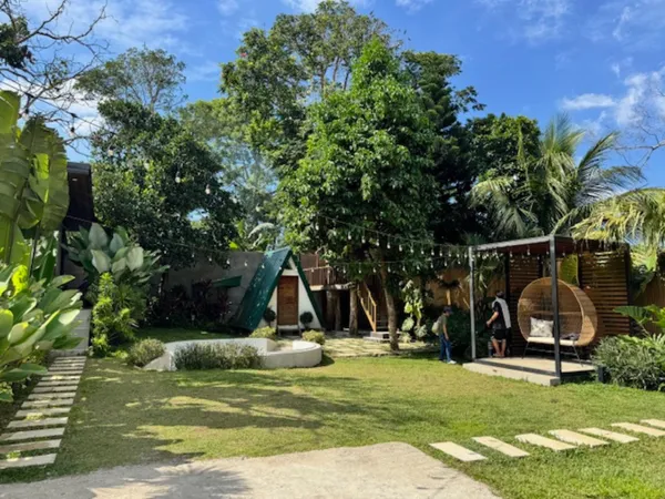 Tropical garden with A-frame cabin, stepping stones, and rattan hanging chairs at R-Escape Silang